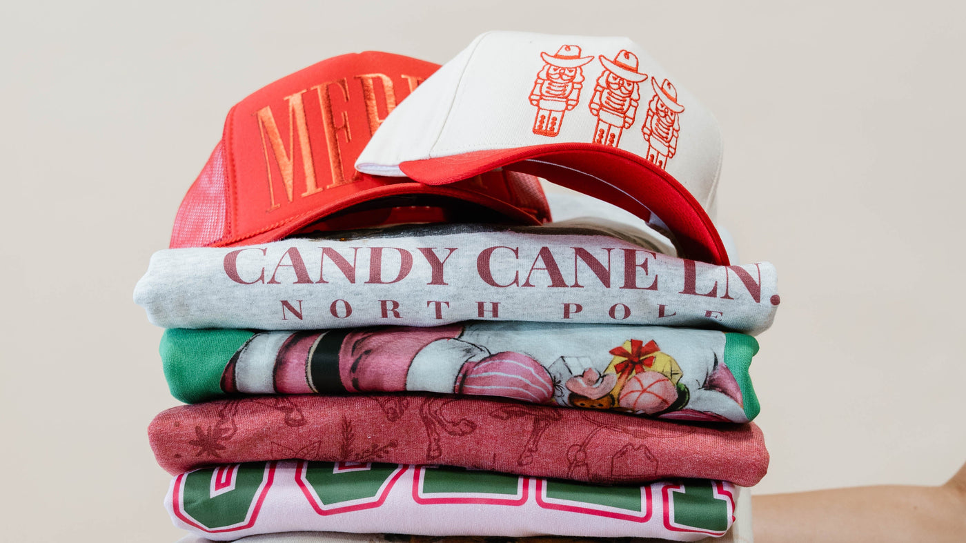 Stack of the new arrival christmas collection pullovers and hats held by a hand against a plain background.